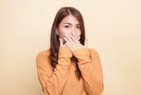 Beautiful young Asian woman close her mouth on beige background
