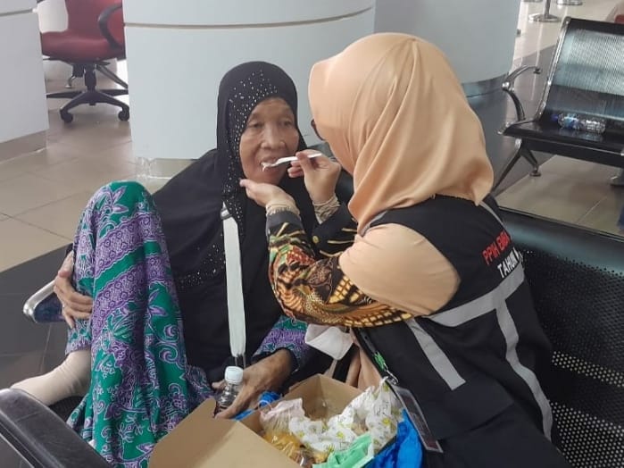 Untuk memastikan keamanan dan keselamatan jemaah dengan risiko tinggi (risti), Yunita Nadia, salah satu petugas PPIH Debarkasi Batam mendampingi pemulangan Kamaliah Kontel, jemaah haji asal Rokan Hilir Riau. Foto: Kemenag Kepri 