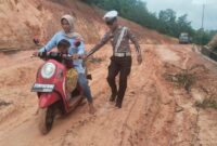 personel Polsek Daik Lingga turun langsung membantu pengendara yang kesulitan melewati jalan rusak dan berlumpur di sekitar Pelabuhan Roro Penarik. Foto: INIKEPRI.COM