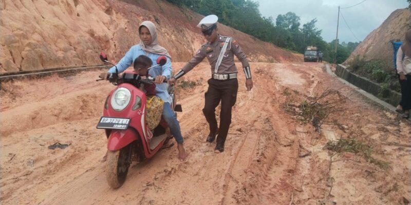 personel Polsek Daik Lingga turun langsung membantu pengendara yang kesulitan melewati jalan rusak dan berlumpur di sekitar Pelabuhan Roro Penarik. Foto: INIKEPRI.COM
