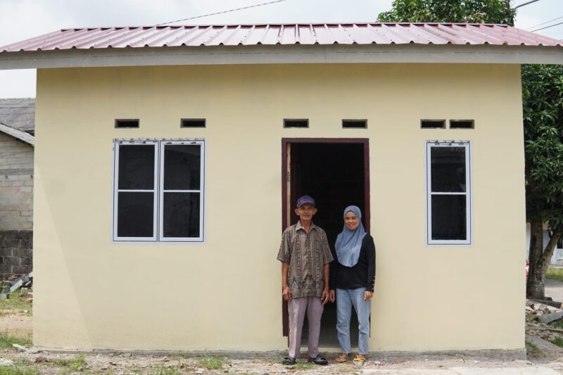 Emat, 77 tahun, bersama putrinya di depan rumah yang dibangun Pemerintah Provinsi Kepri melalui Dinas Perkim di Toapaya Selatan, Kecamatan Toapaya, Kabupaten Bintan. Foto: INIKEPRI.COM/KepriProv 