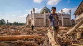 Seorang anak berjalan di depan masjid pasca bencana banjir bandang. Foto: BBC